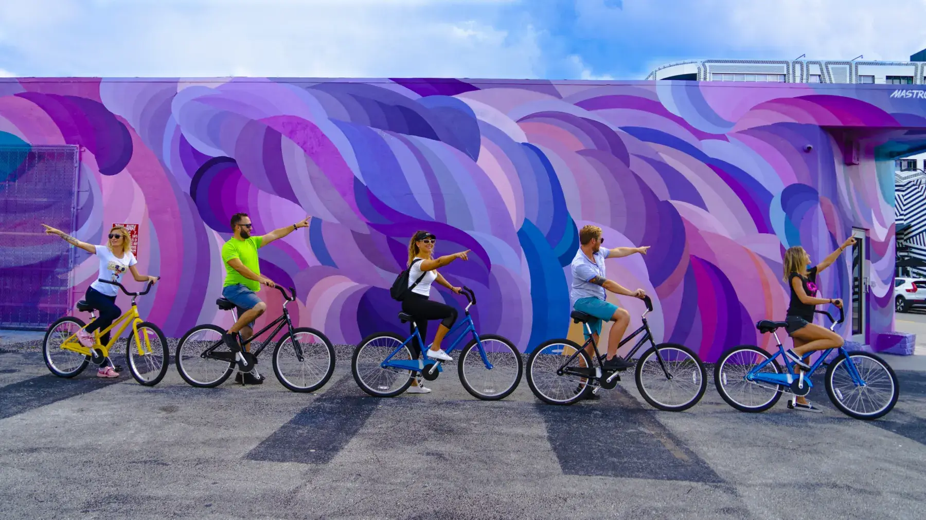 Two riders on beach cruisers alongside a purple wave mural