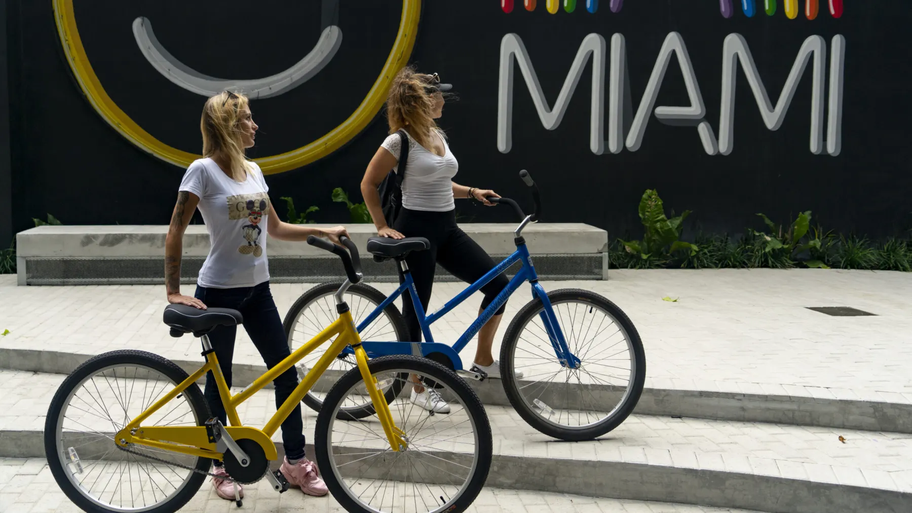 Two riders on beach cruisers passing a bright street mural