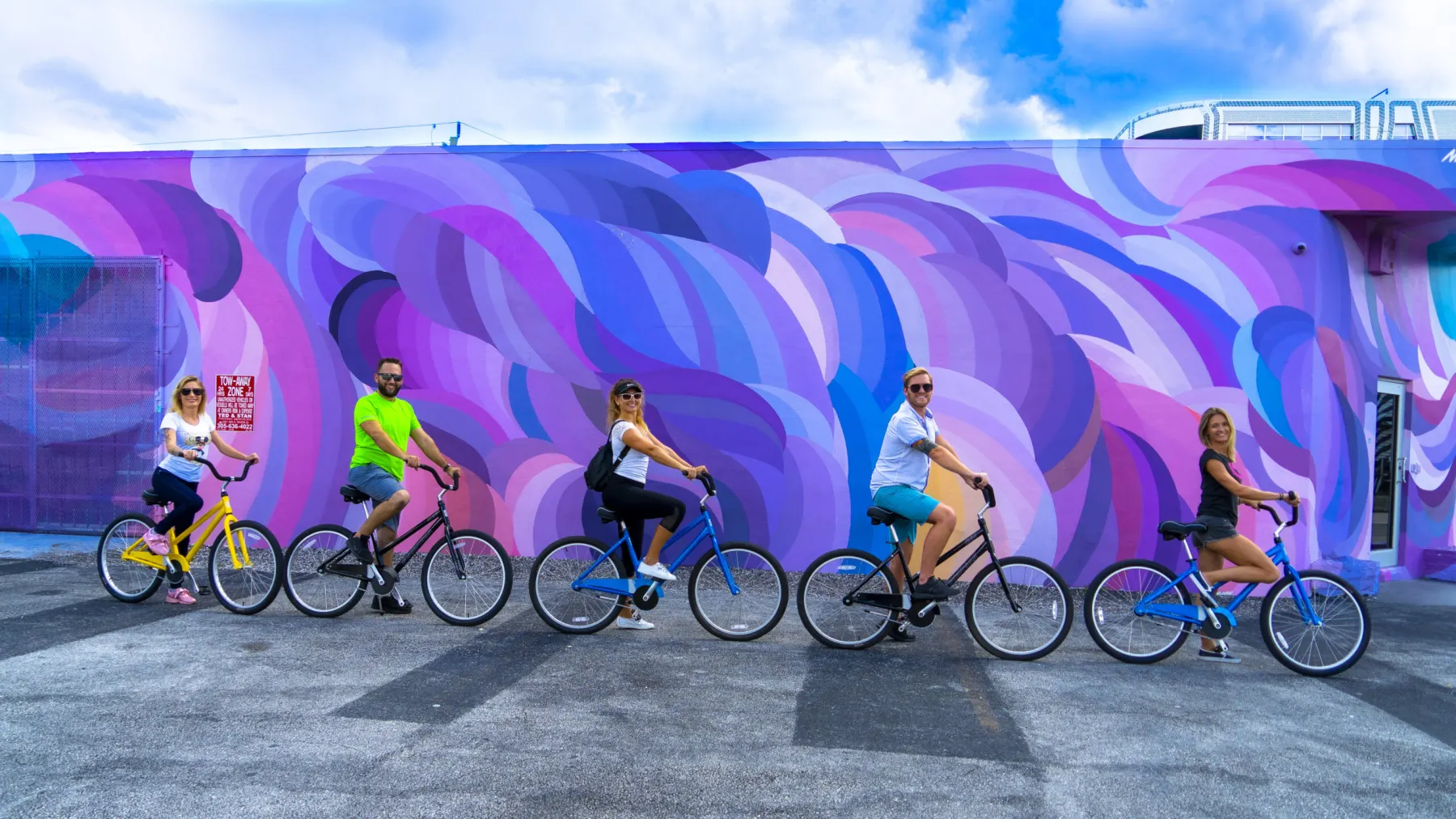 Riders on beach cruisers passing a purple and blue wave mural