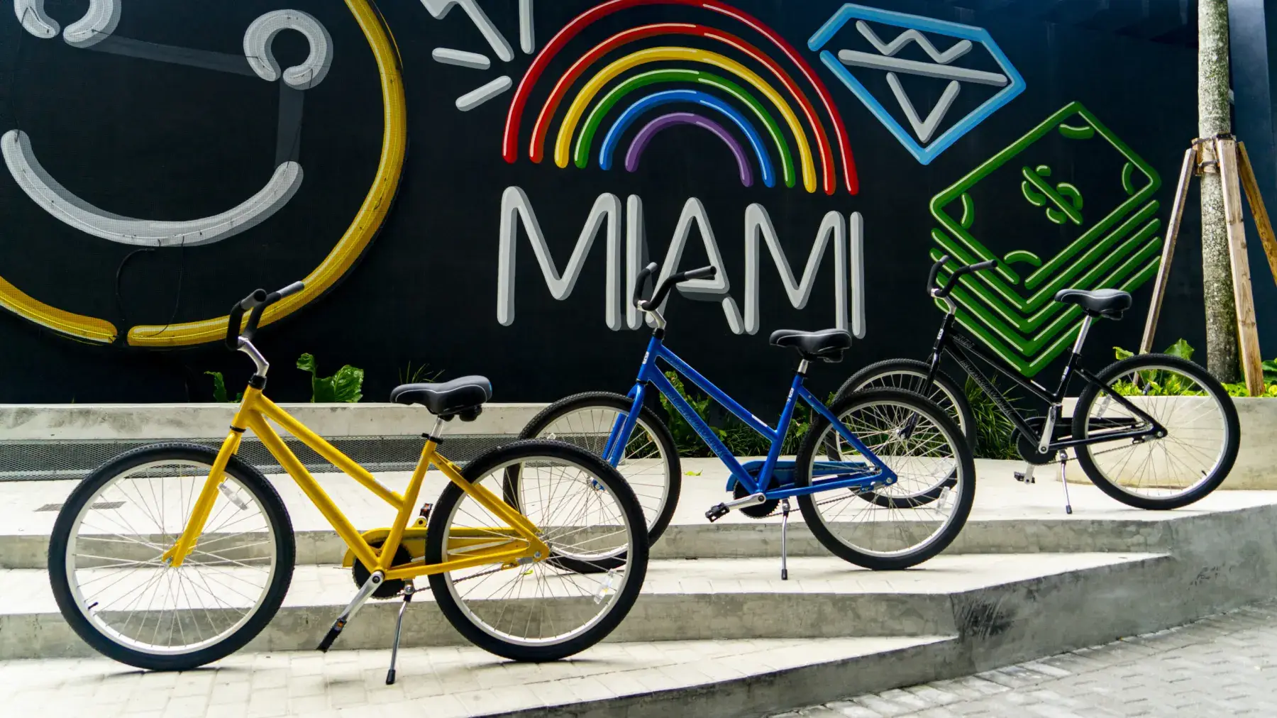 A yellow and a blue beach cruiser parked in front of a colourful Miami mural